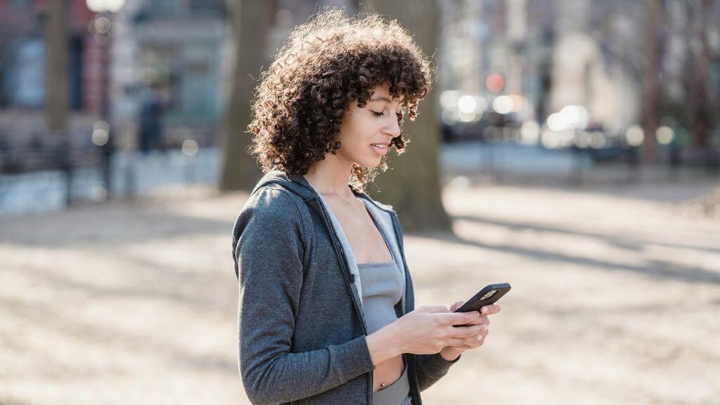 personne dans la rue regardant son téléphone en souriant.